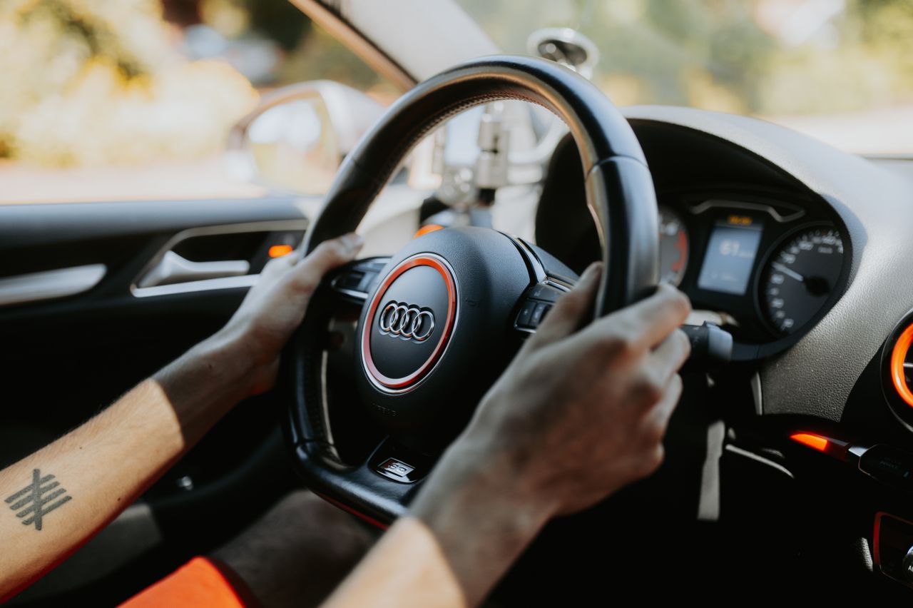gallery-1 A close-up view of hands gripping a car steering wheel with dashboard visible.