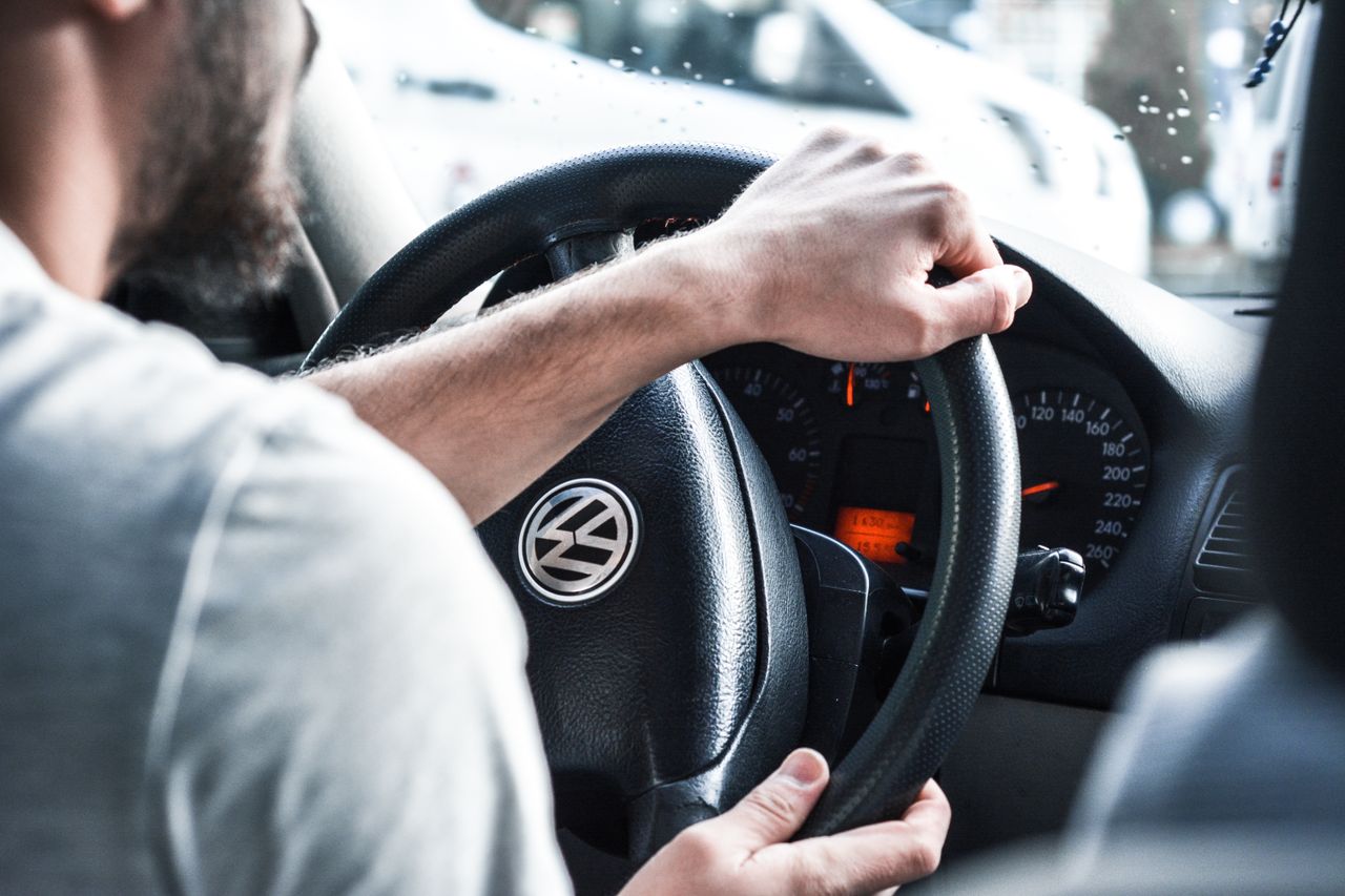 gallery-2 Man gripping Volkswagen steering wheel, focused on driving and vehicle interior details.