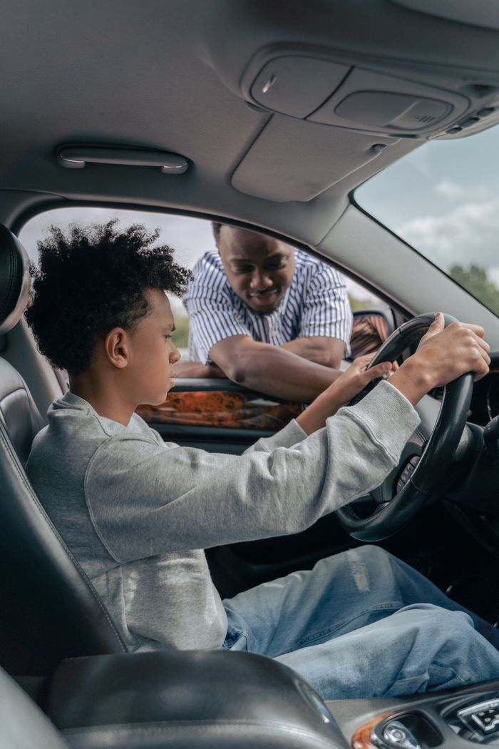 about-02 A father instructing his son on driving inside a car, focusing on the steering wheel.
